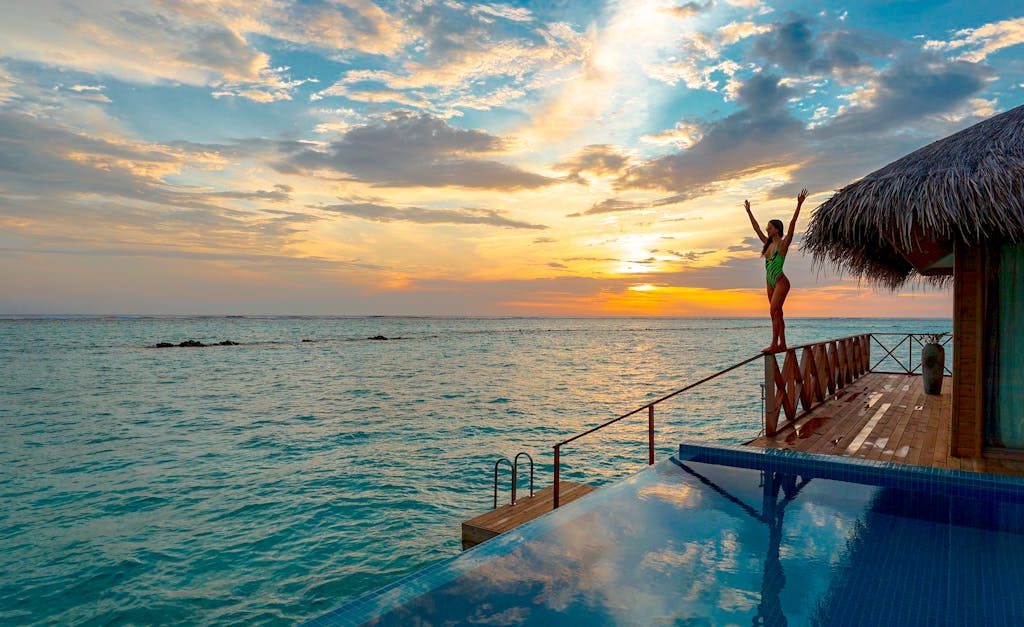 Woman enjoying a stunning sunset at a luxury Maldives resort's infinity pool.