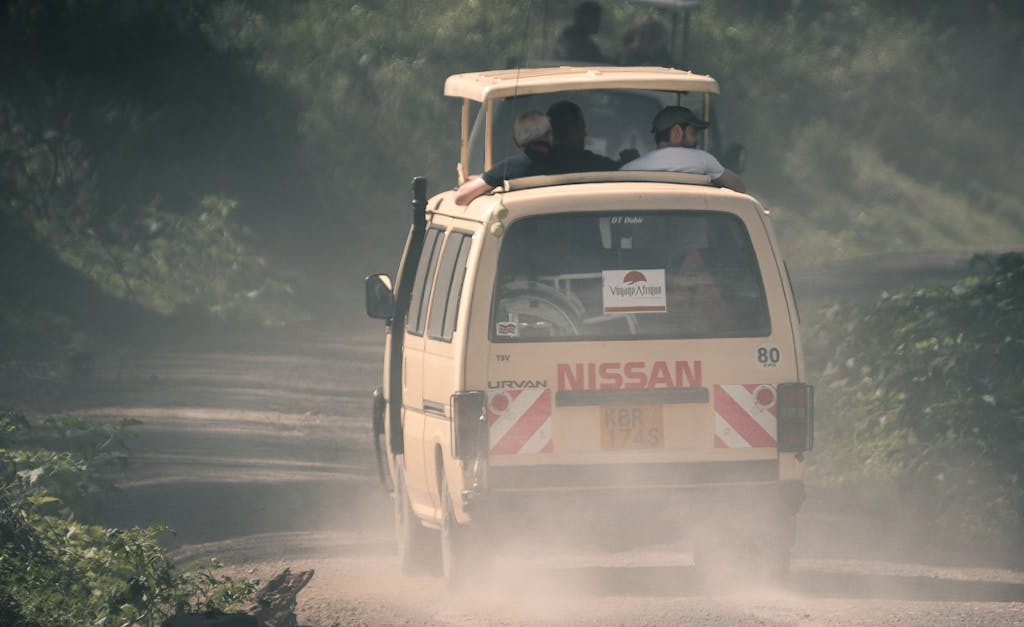 A safari van travels along a misty, unpaved road in Kenya's lush wilderness.
