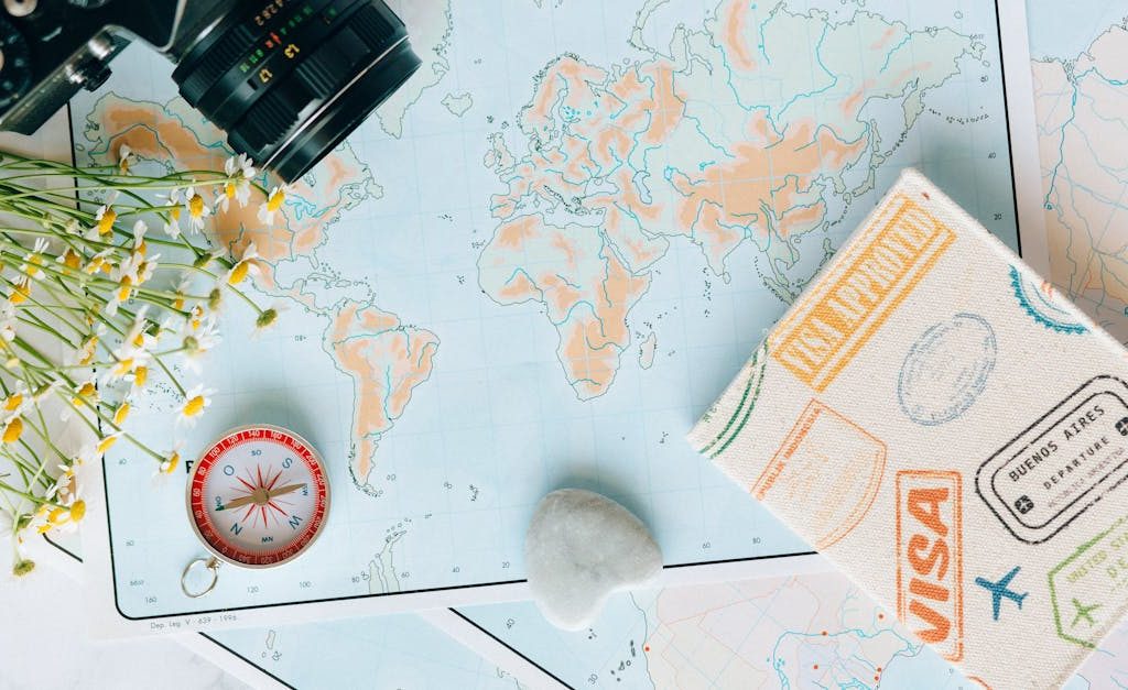 Flat lay of travel essentials: maps, camera, compass, and travel journal for planning adventures.
