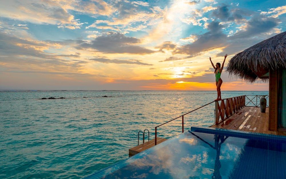 Woman enjoying a stunning sunset at a luxury Maldives resort's infinity pool.